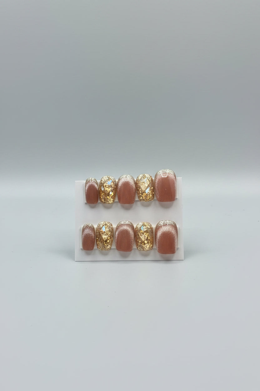 A set of handmade press-on nails displayed on a white card labeled 'Dream Styles HANDMADE NAILS.' The nails have a glossy nude-pink base with alternating clear rhinestone-covered and gold-glittered sections.