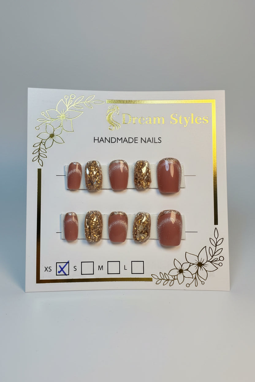 A set of 10 press-on nails displayed on a white card labeled 'Dream Styles HANDMADE NAILS'. The nails feature a glossy mauve-brown base with some decorated in gold glitter and a few with small blue rhinestone accents.