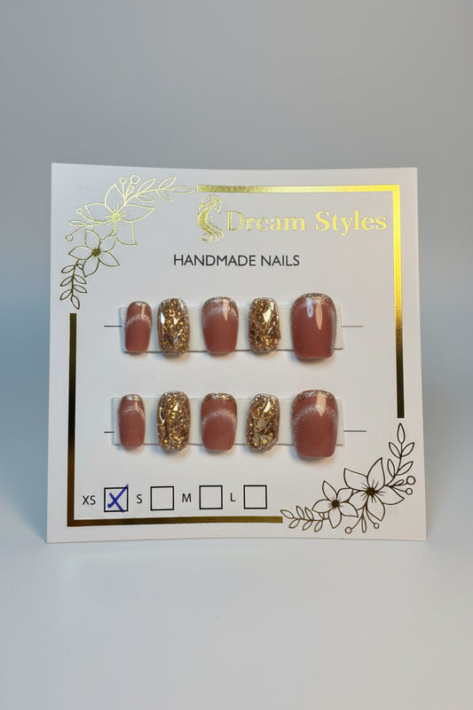 A set of 10 press-on nails displayed on a white card labeled 'Dream Styles HANDMADE NAILS'. The nails feature a glossy mauve-brown base with some decorated in gold glitter and a few with small blue rhinestone accents.