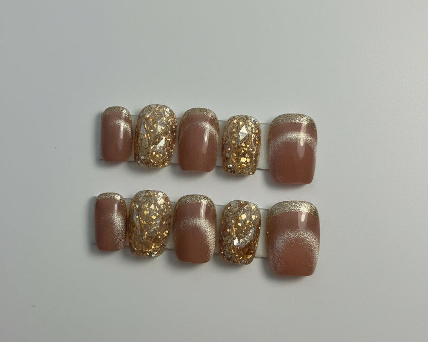 A set of 10 press-on nails displayed on a white card labeled 'Dream Styles HANDMADE NAILS'. The nails feature a glossy mauve-brown base with alternating sections of shimmering gold glitter and a white cat-eye magnetic finish.